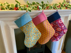 Three colorful Christmas stockings hanging on a fireplace mantle with decorative garland.