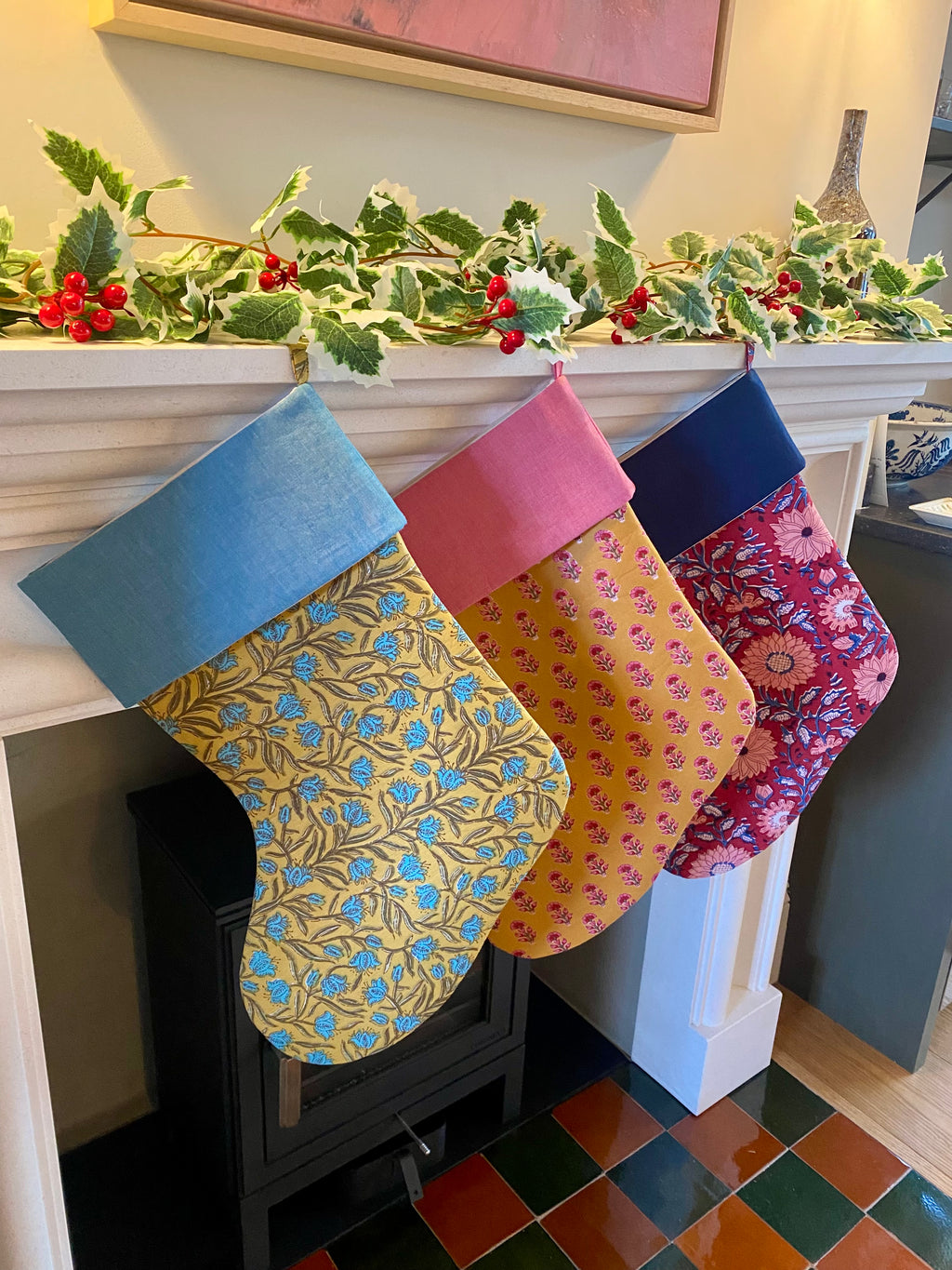 Three patterned stockings hanging on a fireplace mantle with holly decorations.