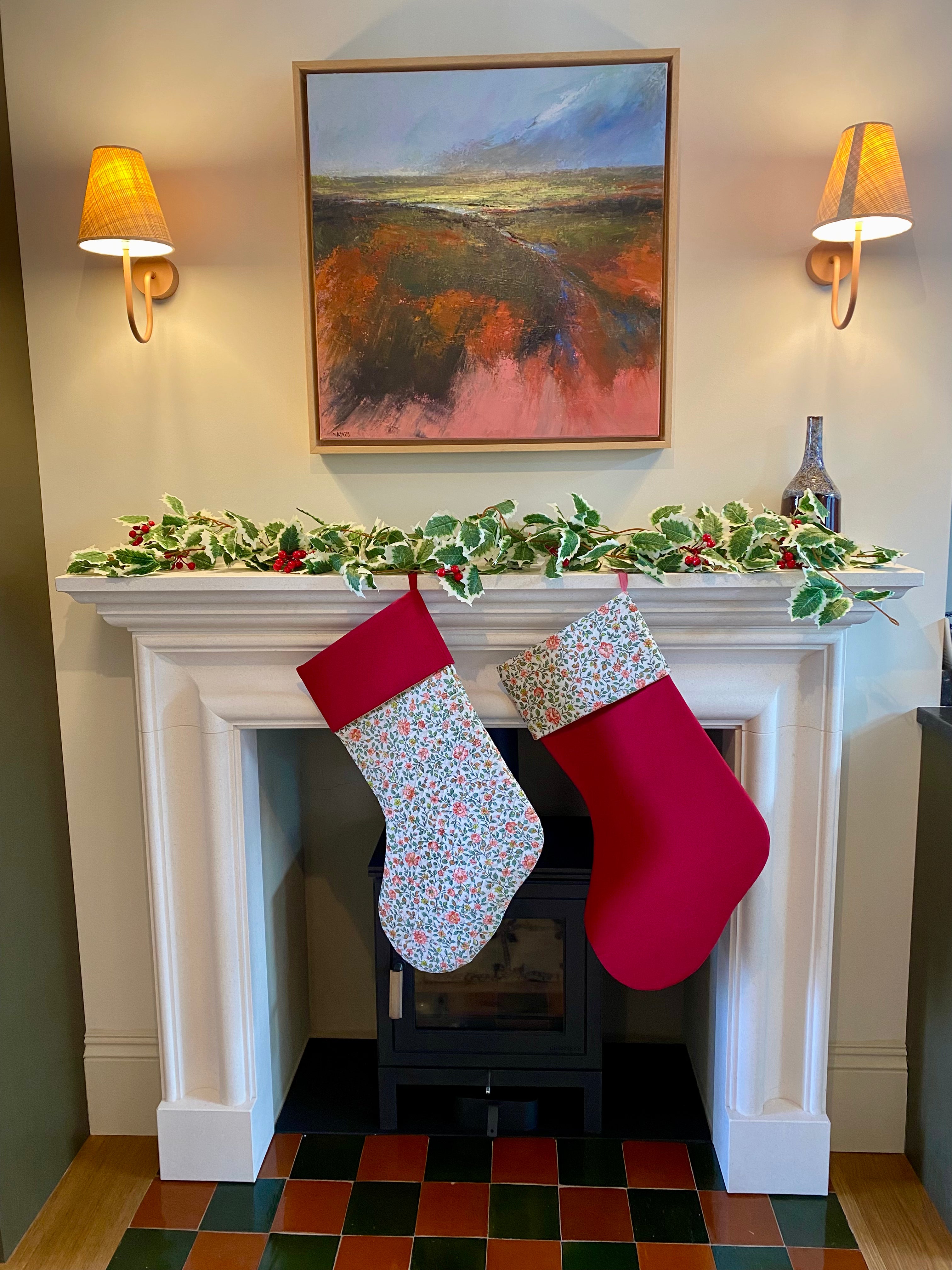 Two quilted Christmas stockings hanging on a fireplace mantle with festive decorations.
