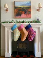 Colorful Christmas stockings hanging on a fireplace mantle with a painting above.