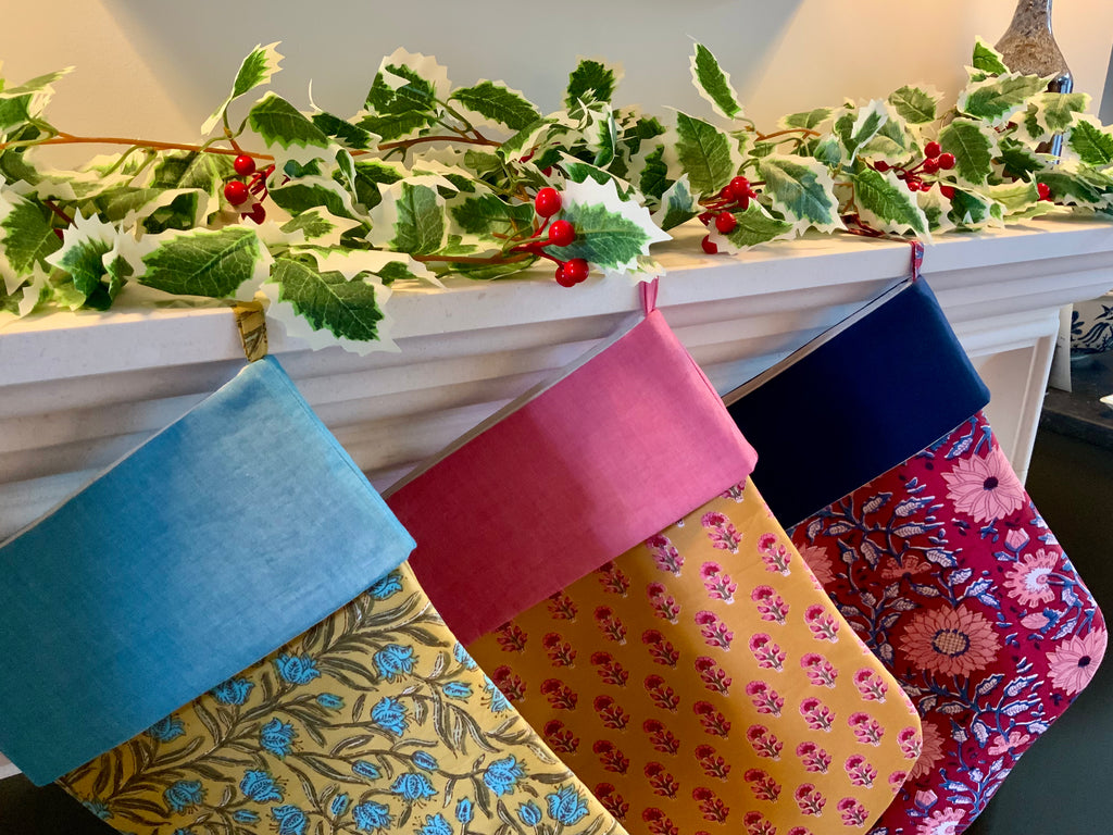 Colorful patterned stockings hanging on a fireplace with holly decorations.