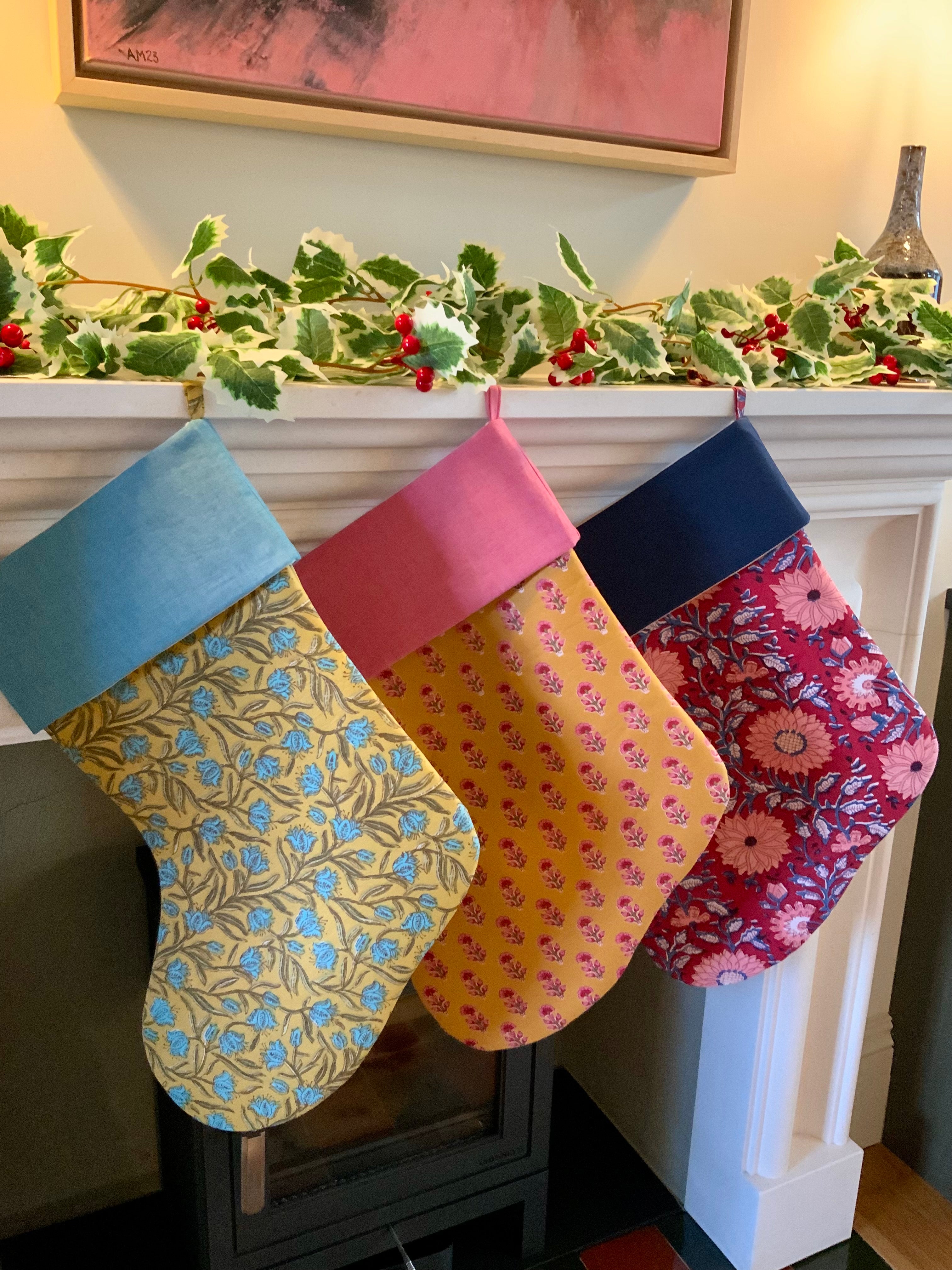 three colorful patterned stockings hanging on a fireplace mantle with holly decorations.