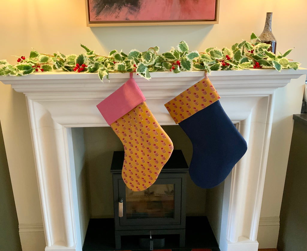 Two Christmas stockings hanging on a fireplace mantel with holly decorations.