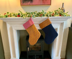 Two Christmas stockings hanging on a fireplace mantel with holly decorations.