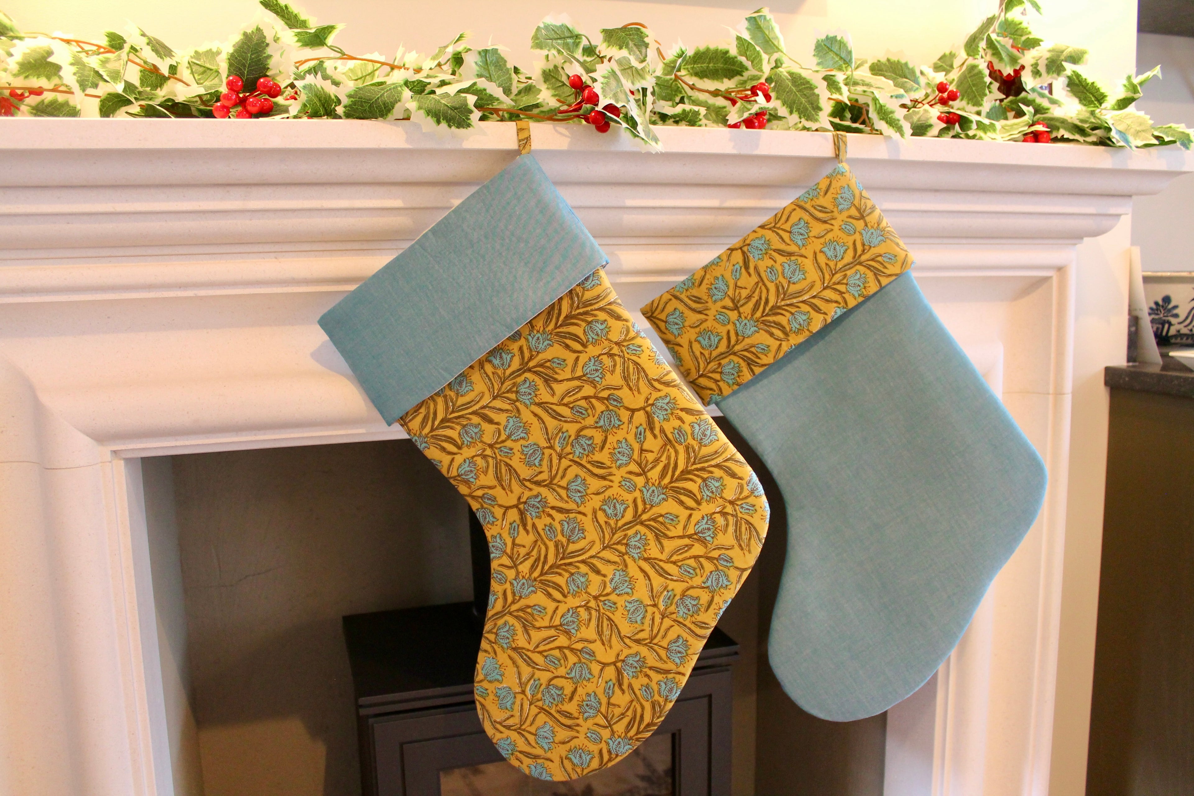 Two Christmas stockings hanging on a fireplace mantle with festive decorations.