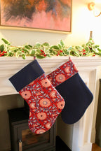 Two Christmas stockings hanging on a fireplace mantle with festive decorations.