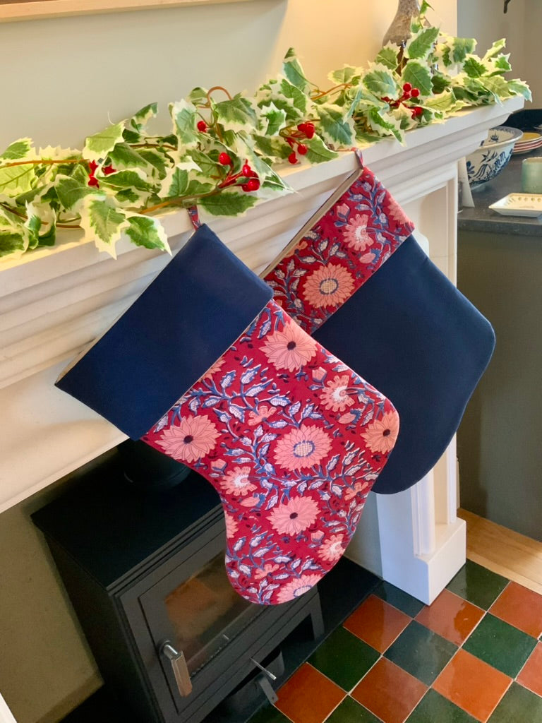 Floral-patterned Christmas stockings hanging on a fireplace mantle with holly decorations.