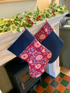 Floral-patterned Christmas stockings hanging on a fireplace mantle with holly decorations.