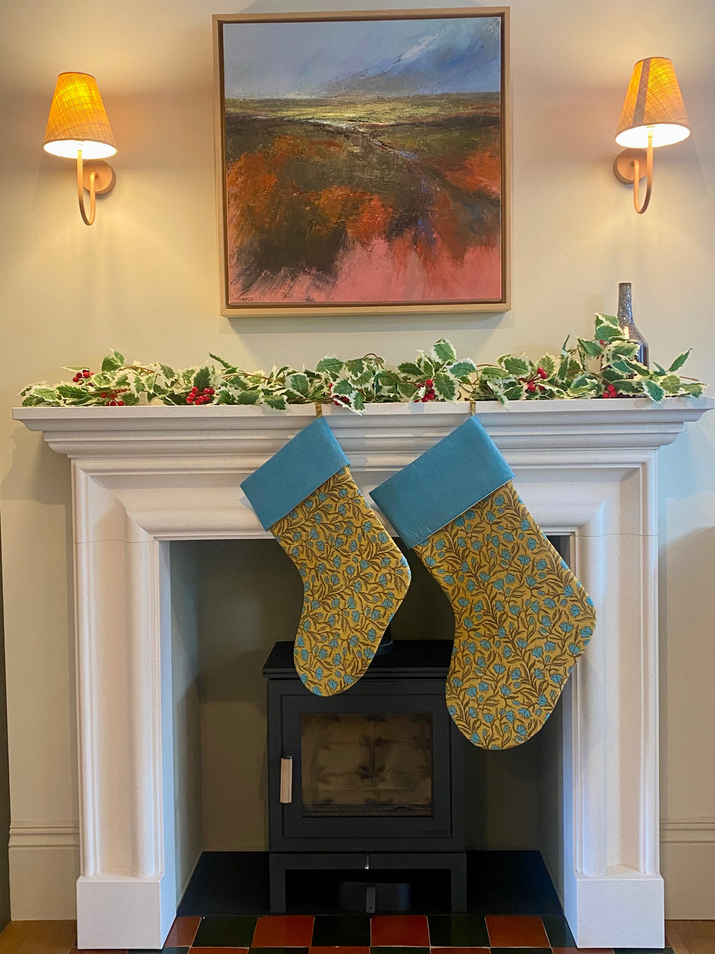 Two Christmas stockings hanging on a fireplace mantel with holly decorations.