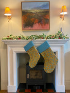 Two Christmas stockings hanging on a fireplace mantel with holly decorations.