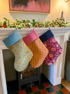 Colorful patterned stockings hanging on a fireplace mantle decorated with holly.