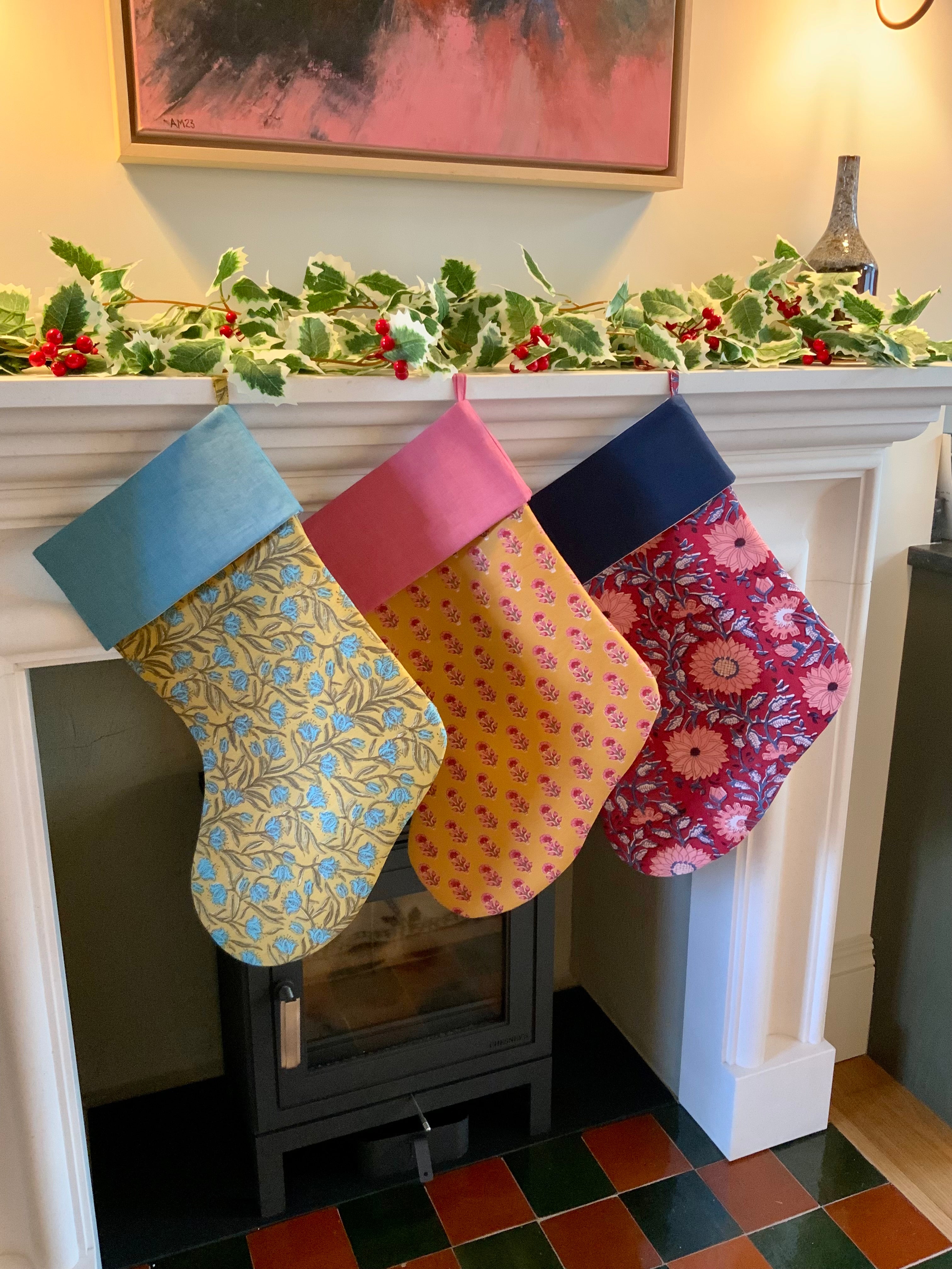 Colorful patterned stockings hanging on a fireplace mantle decorated with holly.