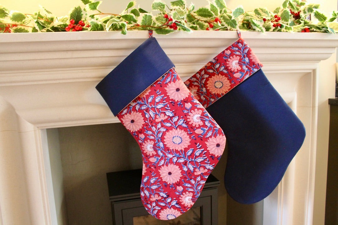 Two Christmas stockings, one floral and one solid blue, hanging on a fireplace mantle.