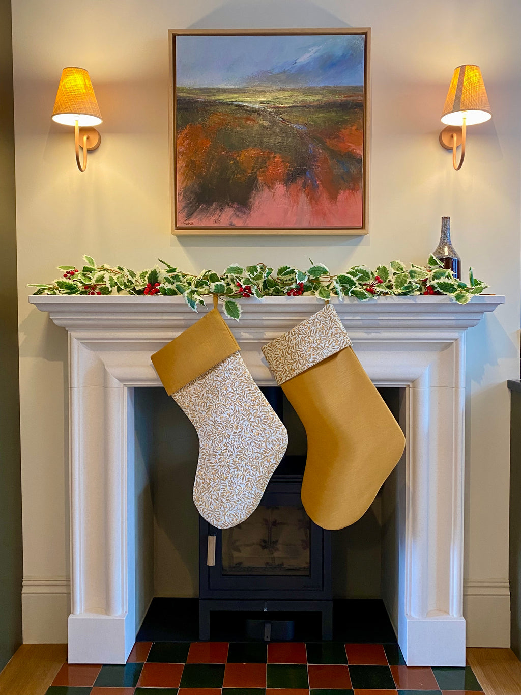 Decorative mantel with Christmas stockings hanging above a fireplace, wall sconces, and a painting.