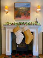 Decorative mantel with Christmas stockings hanging above a fireplace, wall sconces, and a painting.