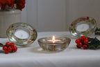 Decorative glass candle holders with floral patterns on a white surface with red berries.