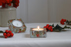 Decorative candles in floral glass holders with berries on a white surface.