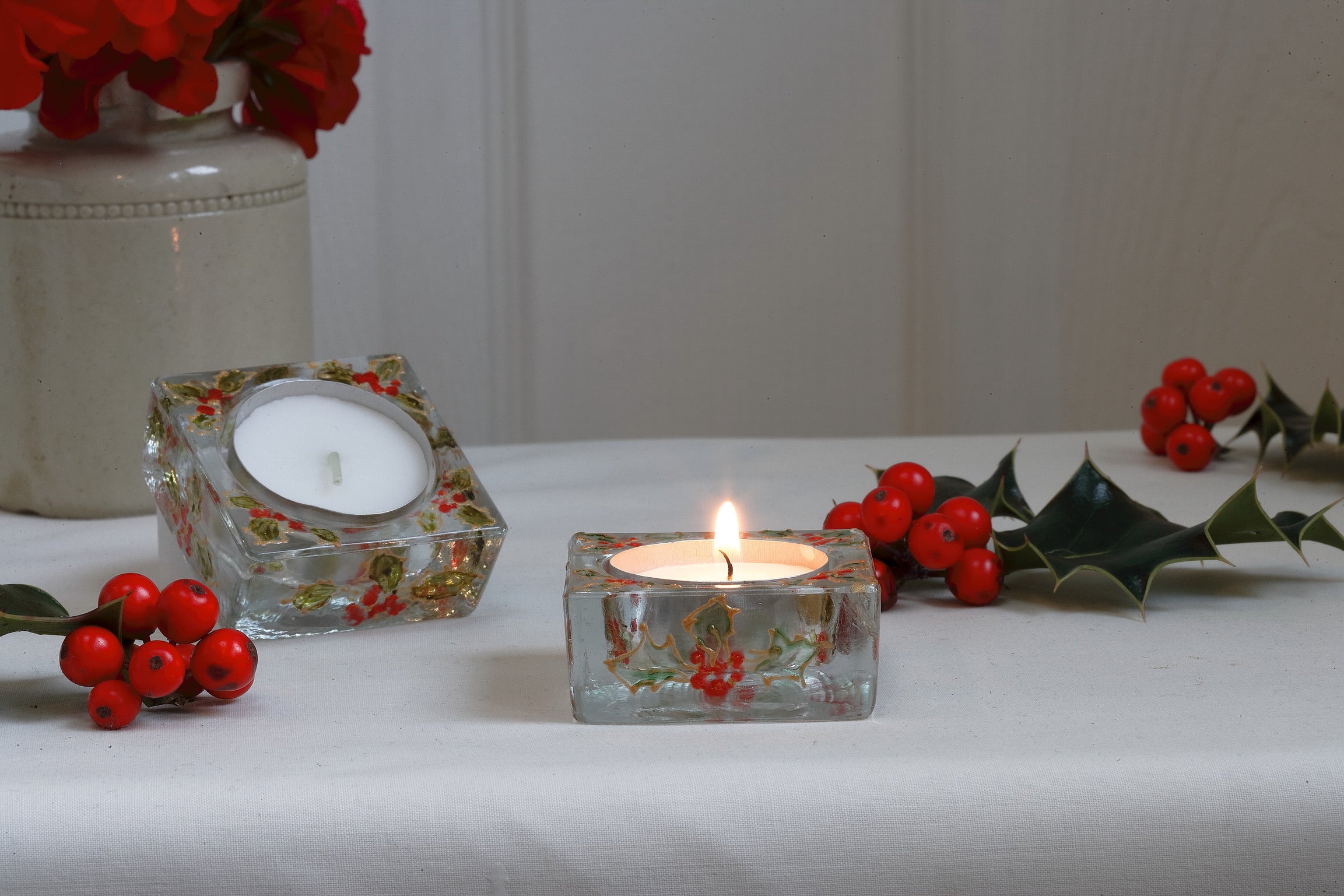 Decorative candles in floral glass holders with berries on a white surface.