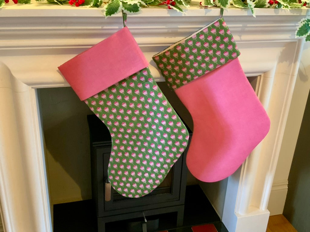 Two Christmas stockings, with a blockprint floral pattern, hanging on a fireplace mantle.
