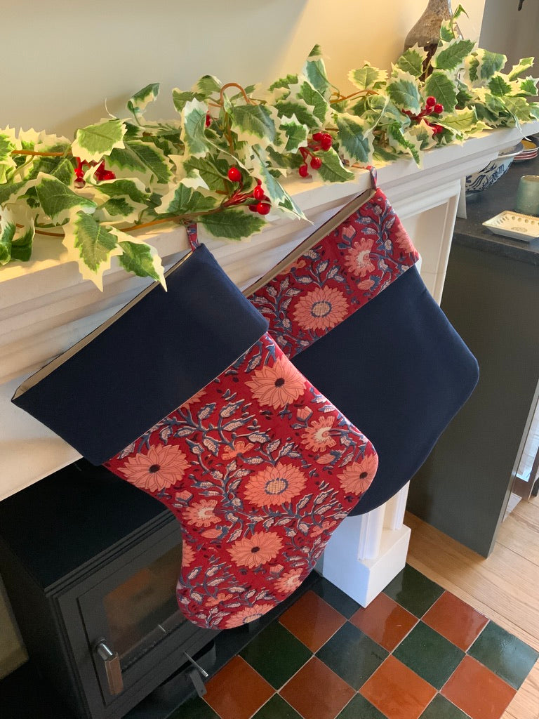 Two Christmas stockings hanging on a fireplace mantle decorated with holly leaves and berries.