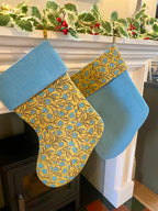 Two Christmas stockings with blue and gold patterns hanging by a fireplace.