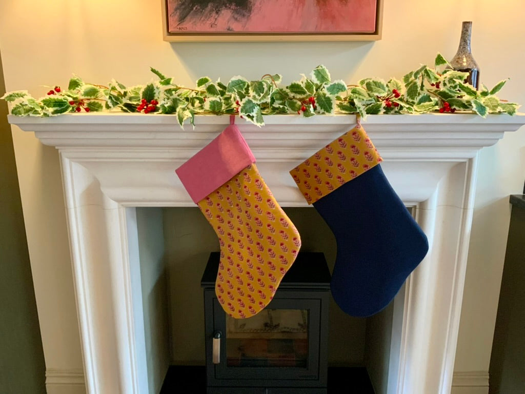 Two colorful stockings hanging on a fireplace mantel with holly decorations.