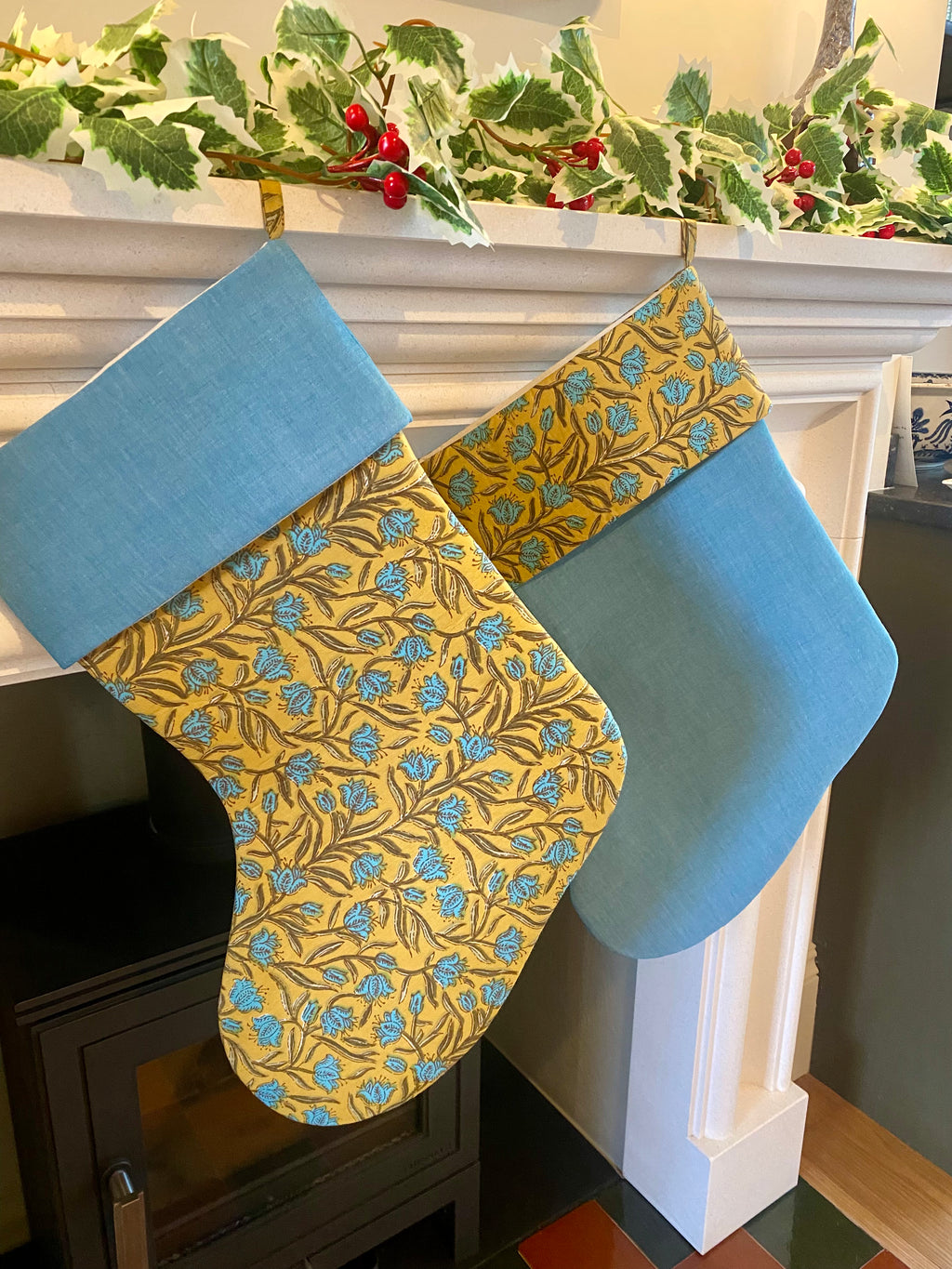 Two Christmas stockings with blue and gold patterns hanging by a fireplace.