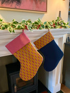 Two Christmas stockings hanging on a fireplace mantle decorated with holly leaves and berries.