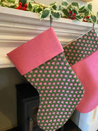 Green Christmas stocking with pink floral pattern hanging on a fireplace mantle.