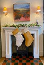 Two quilted Christmas stockings hanging on a fireplace mantle with a painting above.