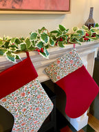 Two quilted Christmas stockings hanging on a fireplace mantle with decorative garland.