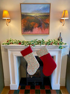 Two Christmas stockings hanging by a fireplace with festive decorations.