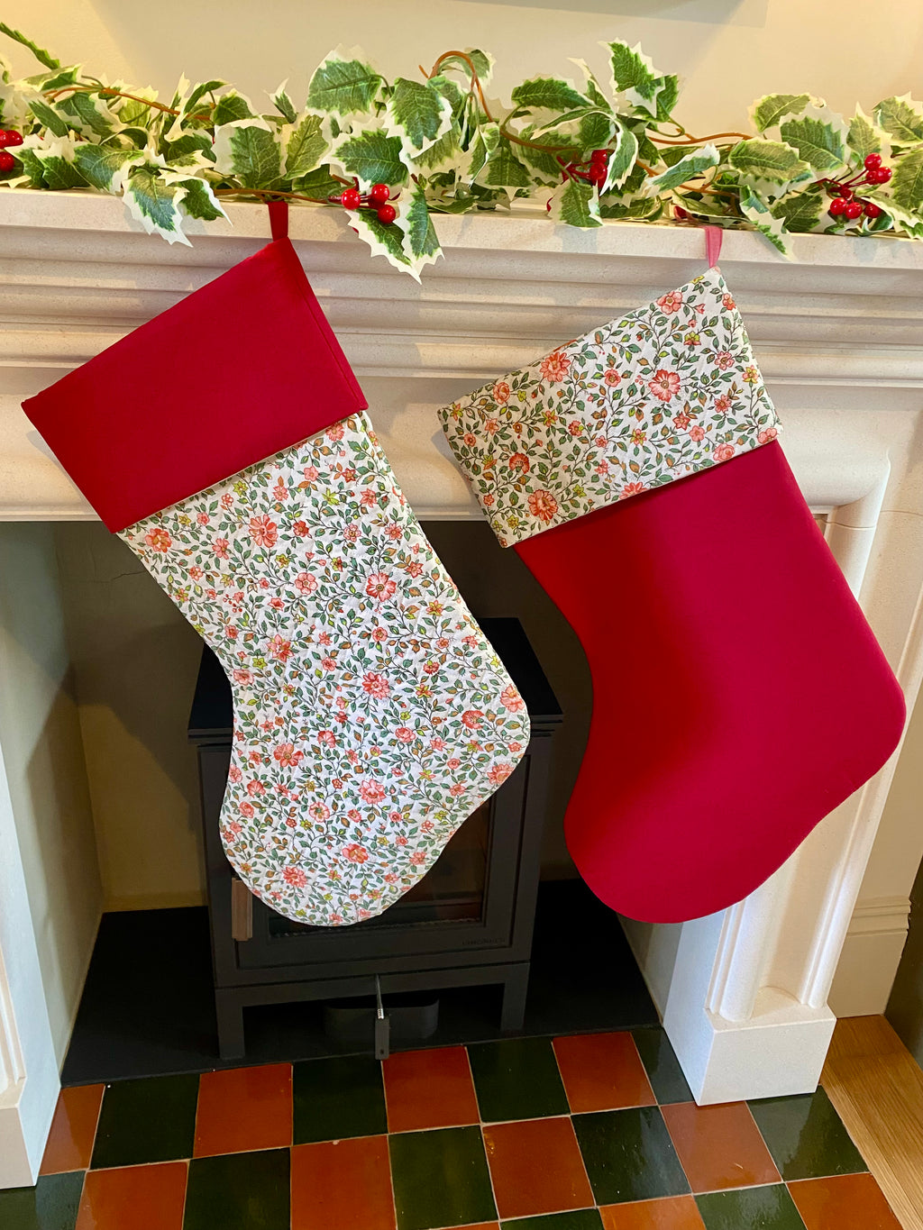 Two Christmas stockings hanging on a fireplace mantle with floral and red patterns.