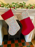 Two Christmas stockings hanging on a fireplace mantle with floral and red patterns.