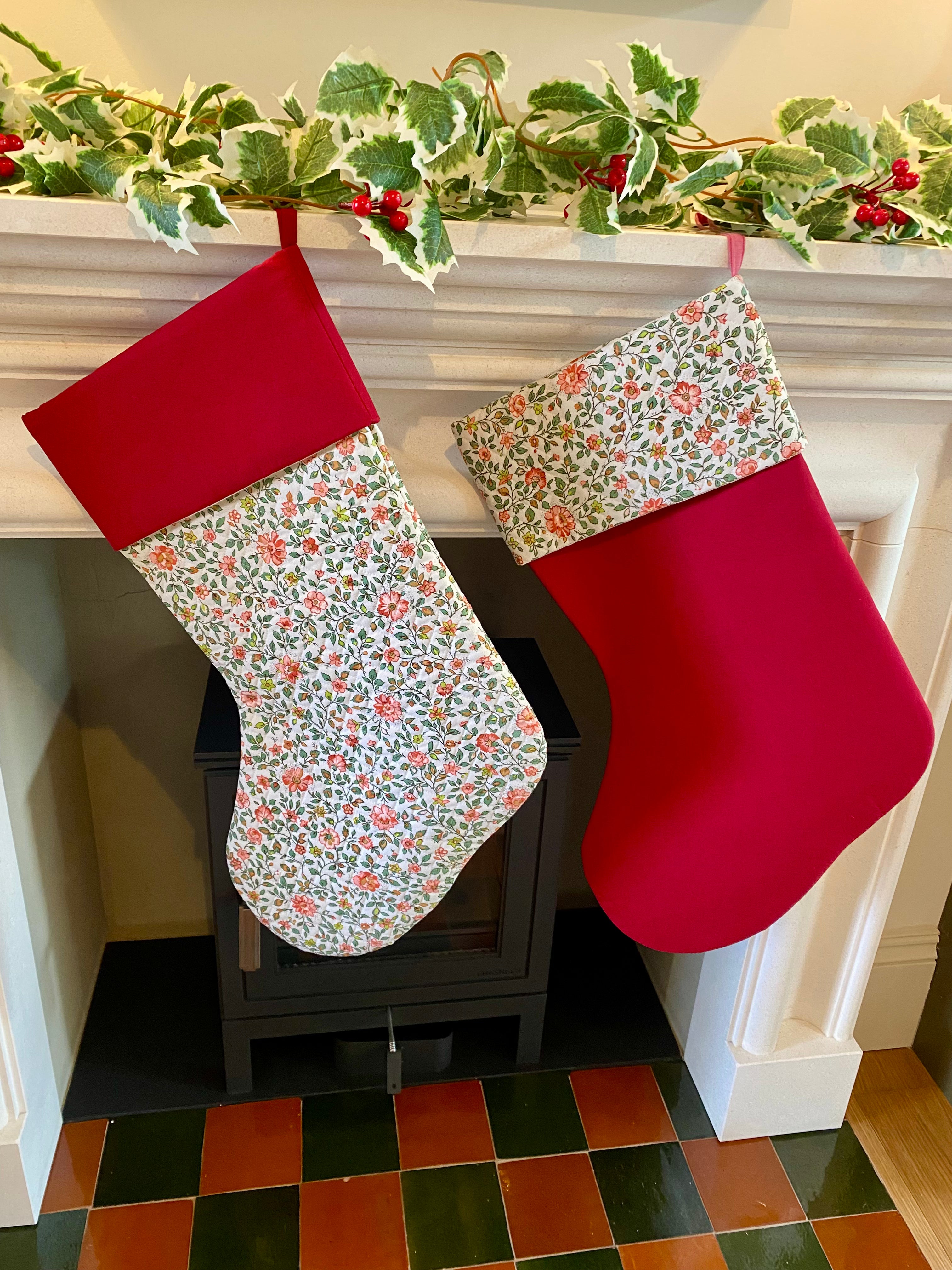 Two Christmas stockings hanging on a fireplace mantle with floral and red patterns.
