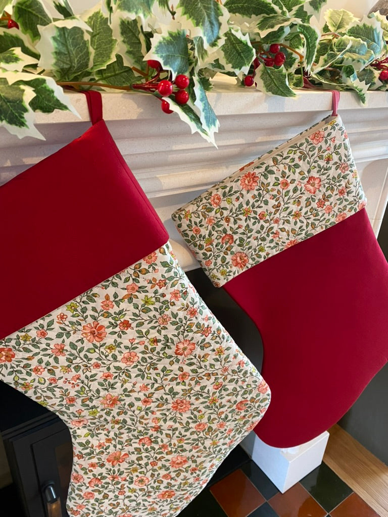 Two floral-patterned Christmas stockings on a fireplace with holly leaves and berries.