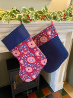 Floral-patterned Christmas stockings hanging on a fireplace mantle with greenery.