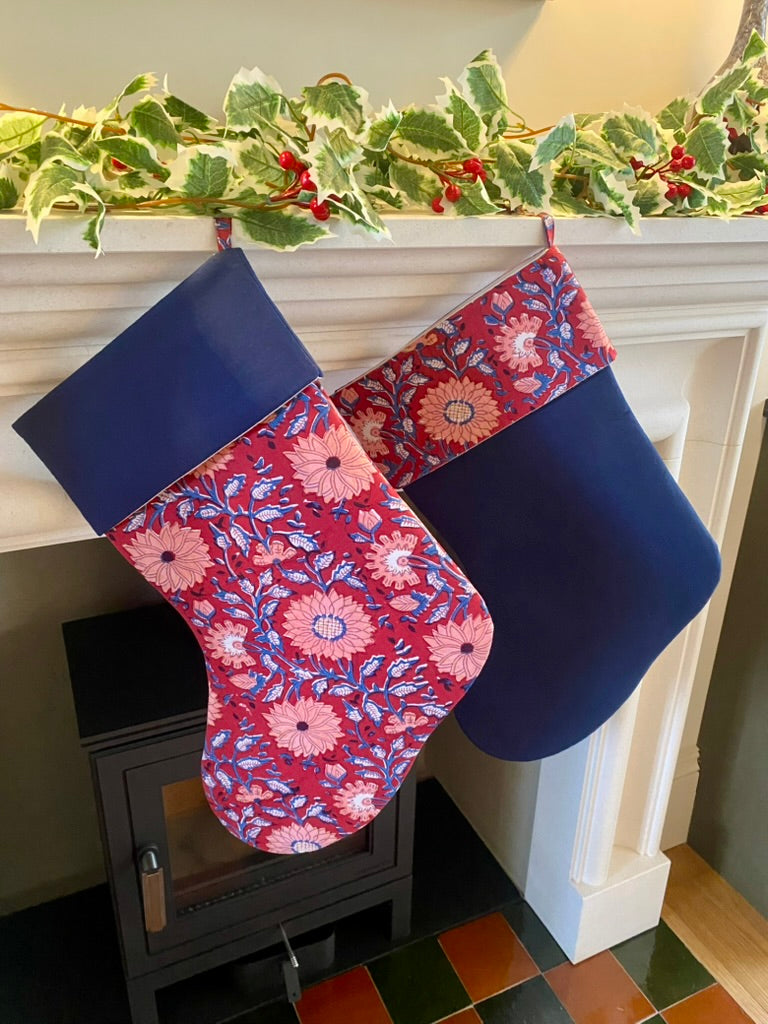Floral-patterned Christmas stockings hanging on a fireplace mantle with greenery.