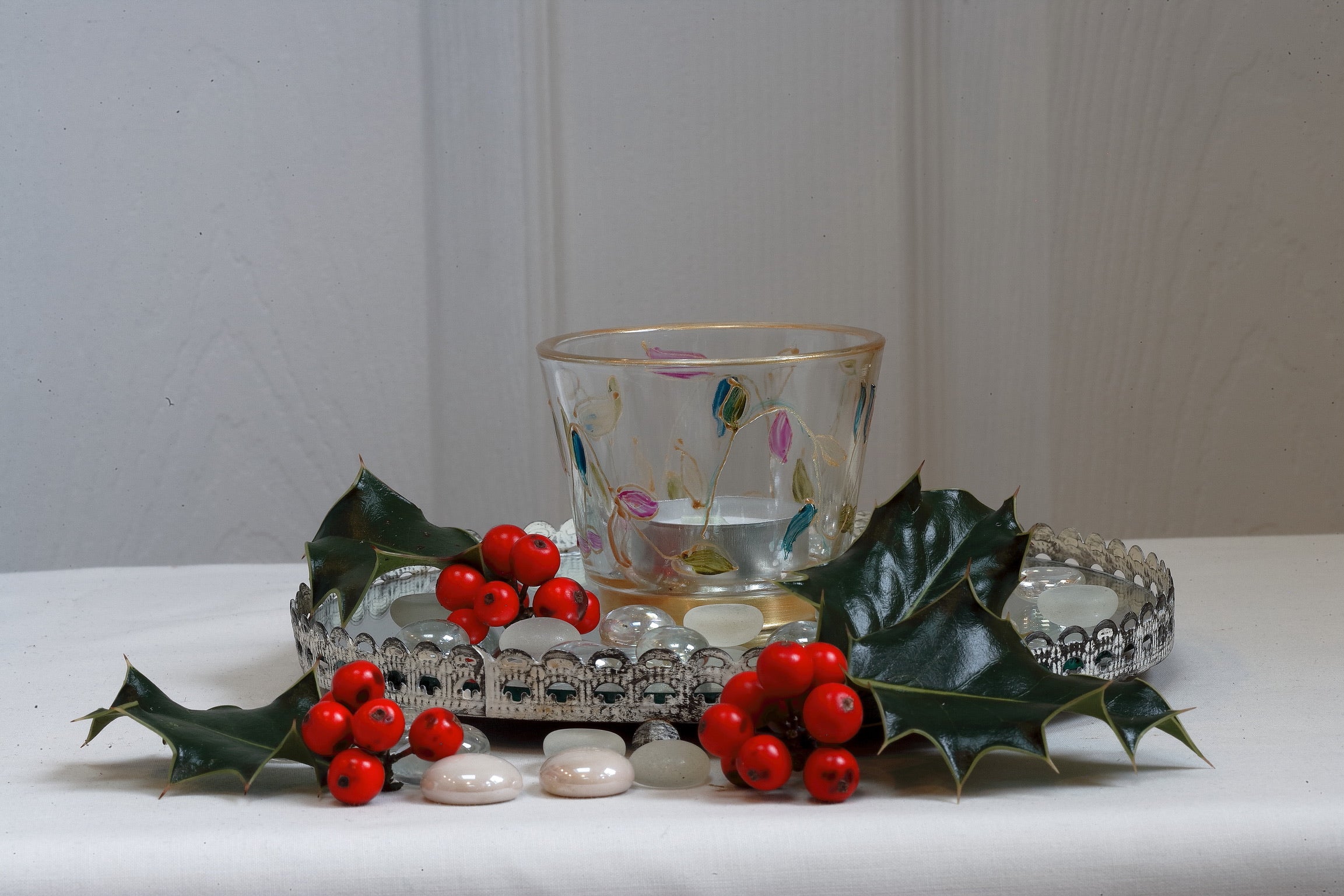 Decorative tealight holder with holly leaves and berries on a white surface