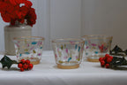 Three glass candle holders with floral designs on a white surface with red berries and green leaves.