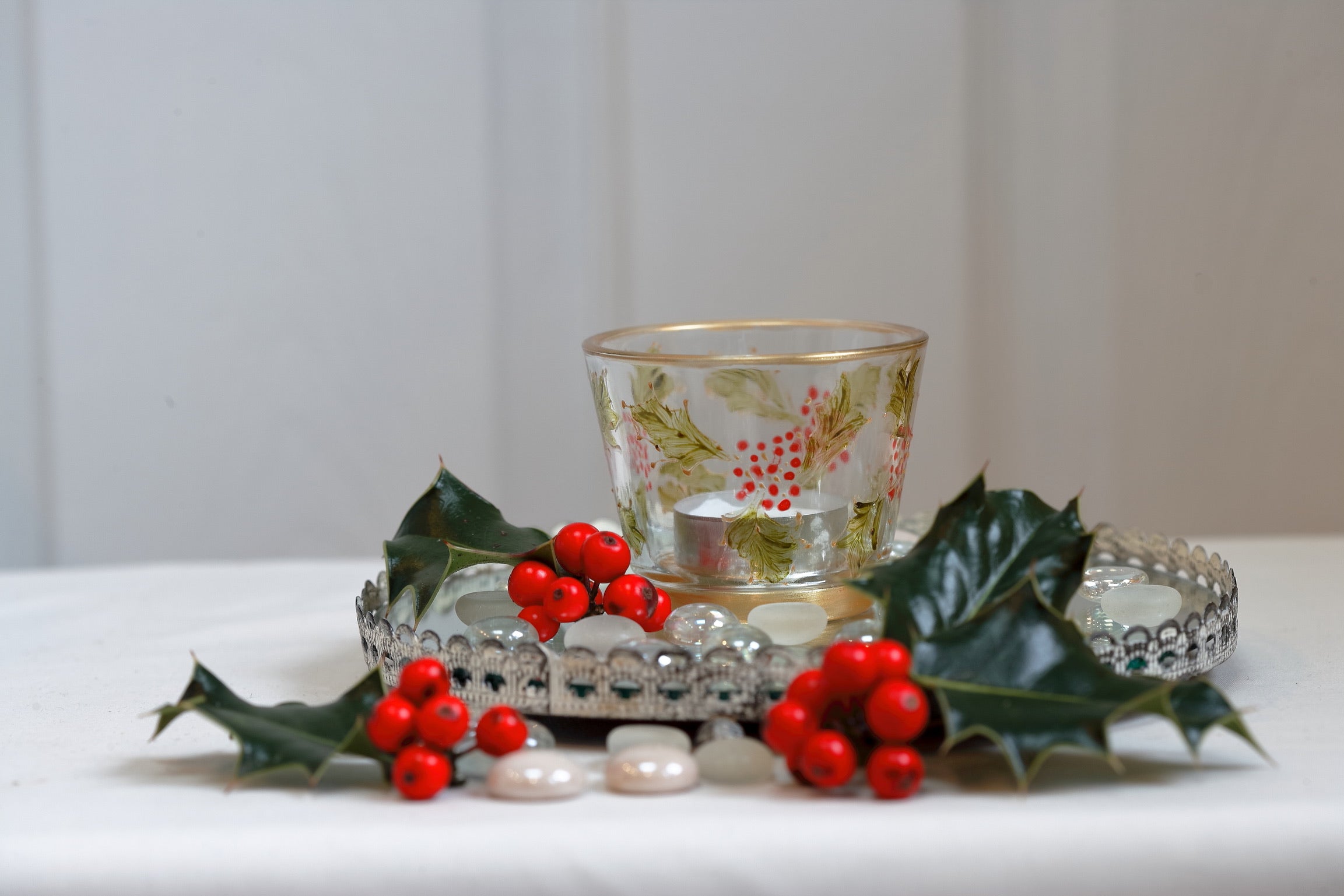 Decorative tealight holder with holly leaves and berries on a white surface