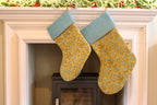 Two Christmas stockings with green and blue patterns hanging on a fireplace mantle.