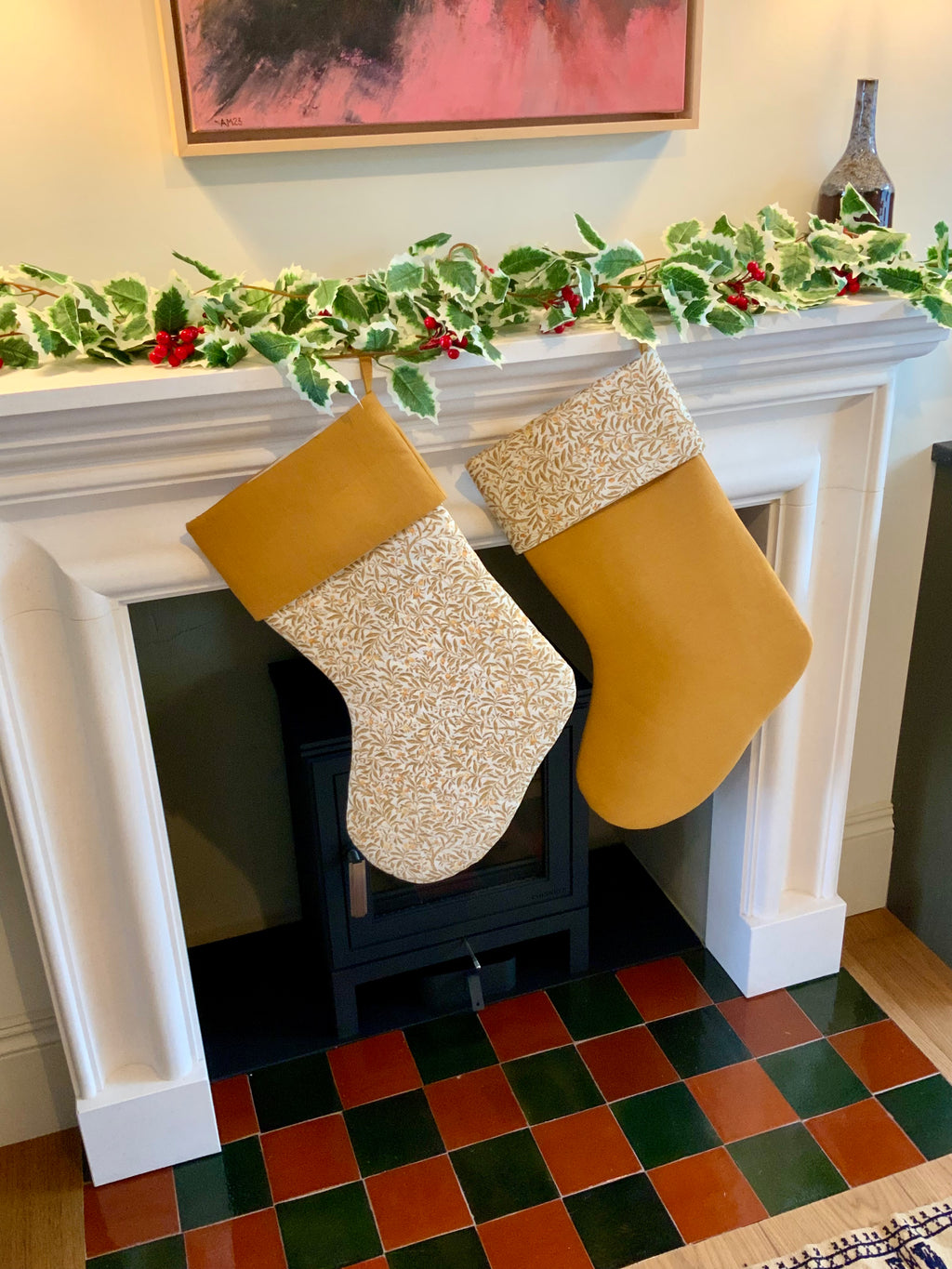 Two yellow floral Christmas stockings hanging on a fireplace mantle decorated with holly leaves and berries.