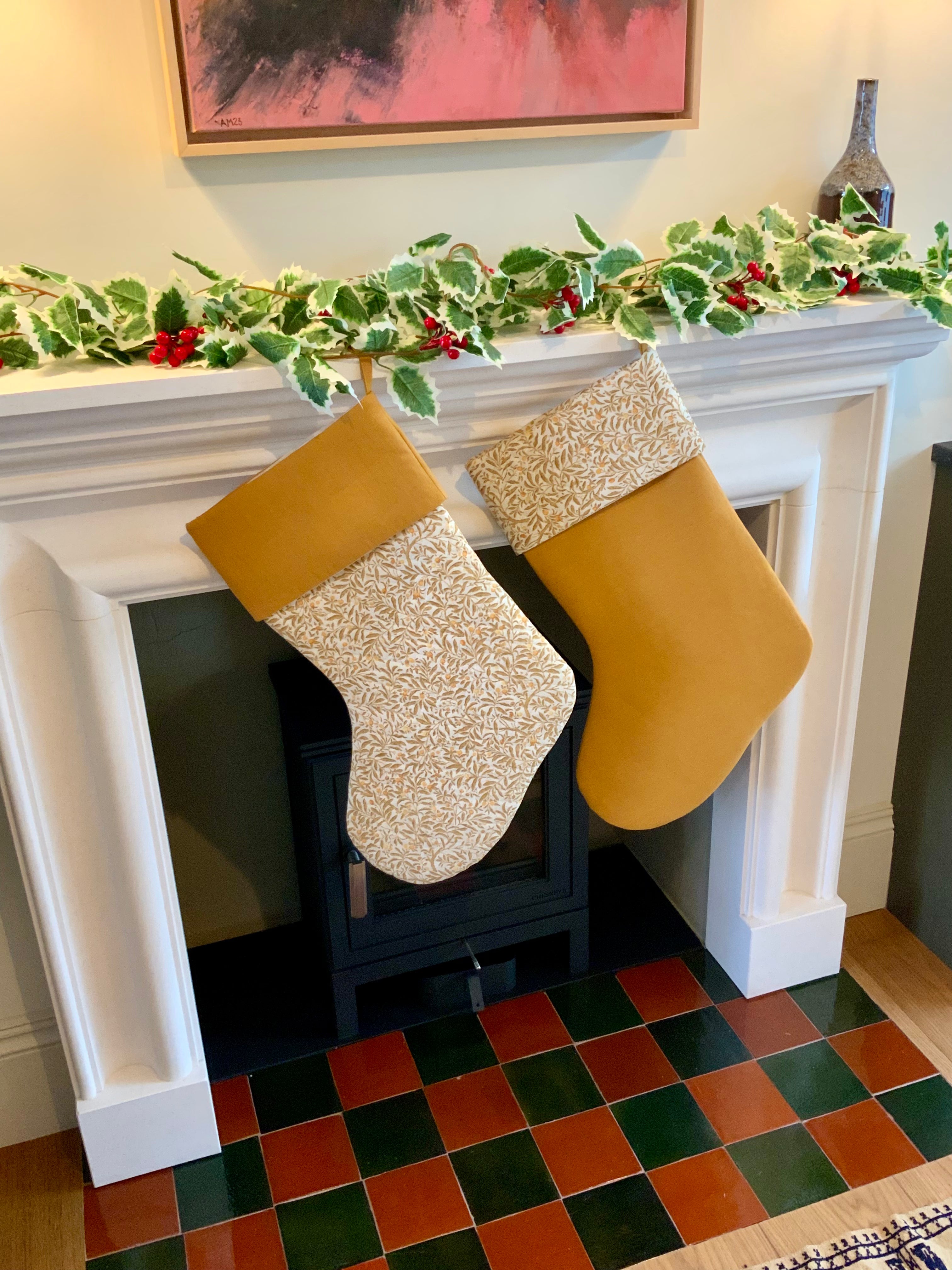 Two yellow floral Christmas stockings hanging on a fireplace mantle decorated with holly leaves and berries.