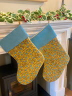 Two yellow patterned stockings with blue trim hanging on a fireplace mantle.