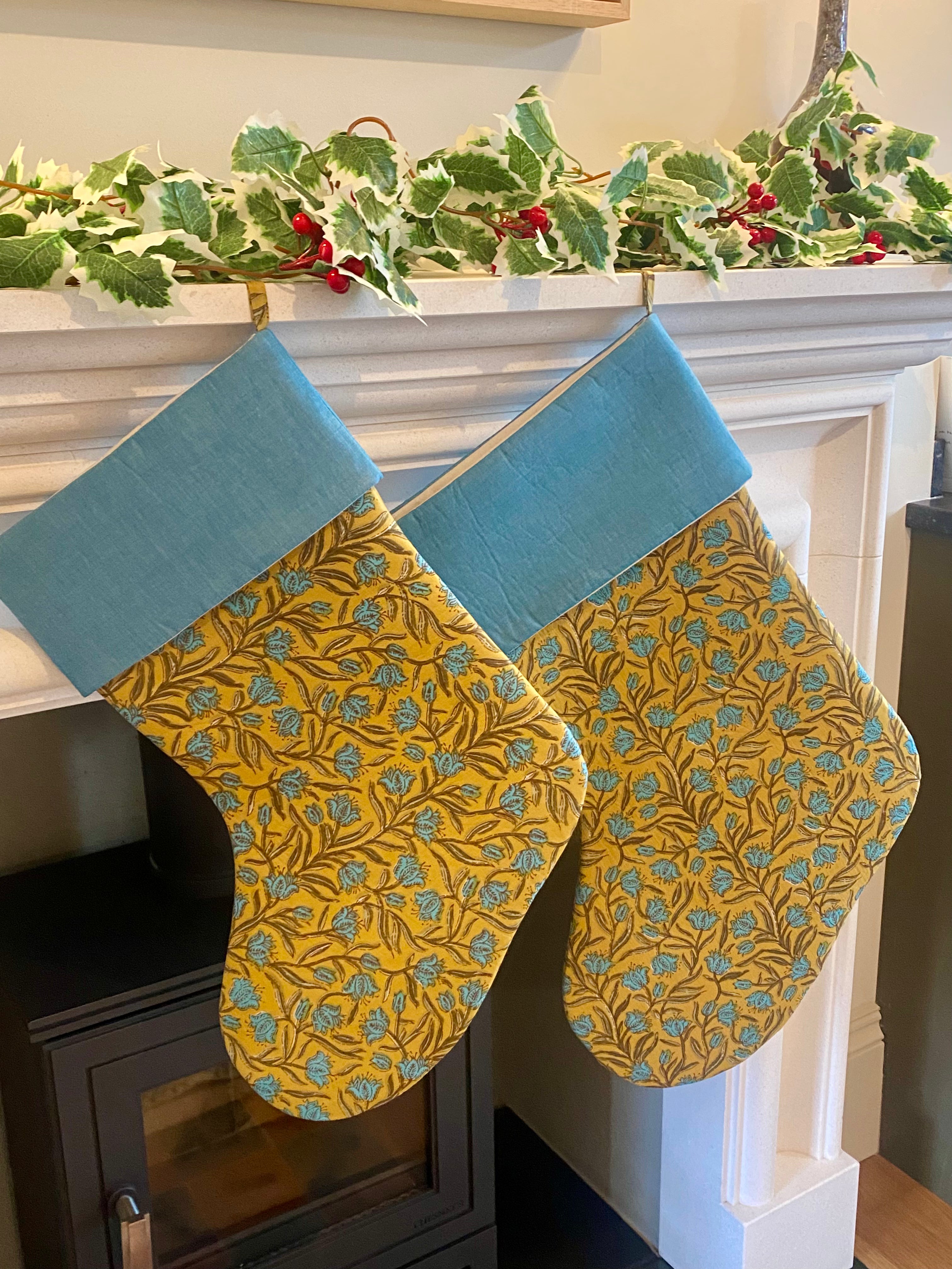 Two yellow patterned stockings with blue trim hanging on a fireplace mantle.